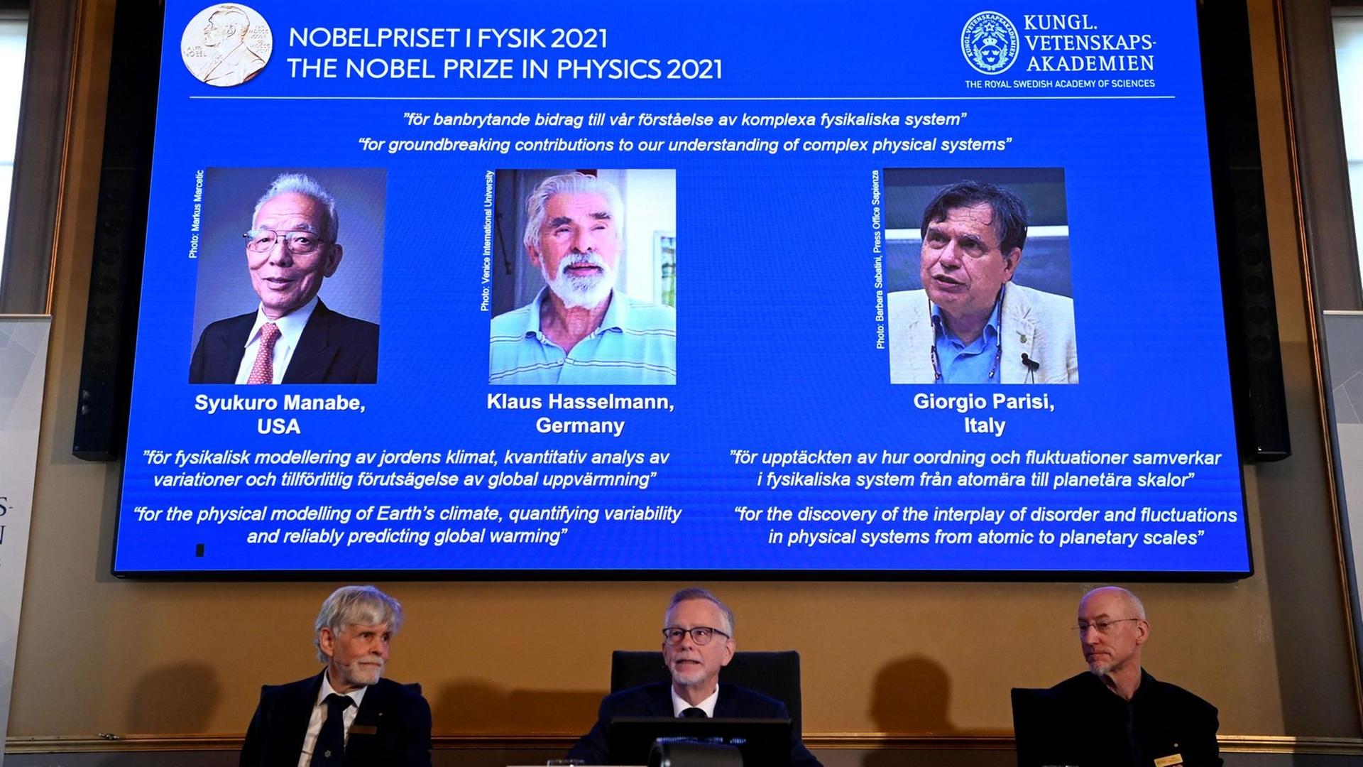 Das schwedische Nobelpreis-Komitee verkündet die Gewinner des Physik-Preises. Hinter ihnen ein Bildschirm mit den drei Gewinnern. Das schwedische Nobelpreis-Komitee verkündet die Gewinner des Physik-Preises. Hinter ihnen ein Bildschirm mit den drei Gewinnern.