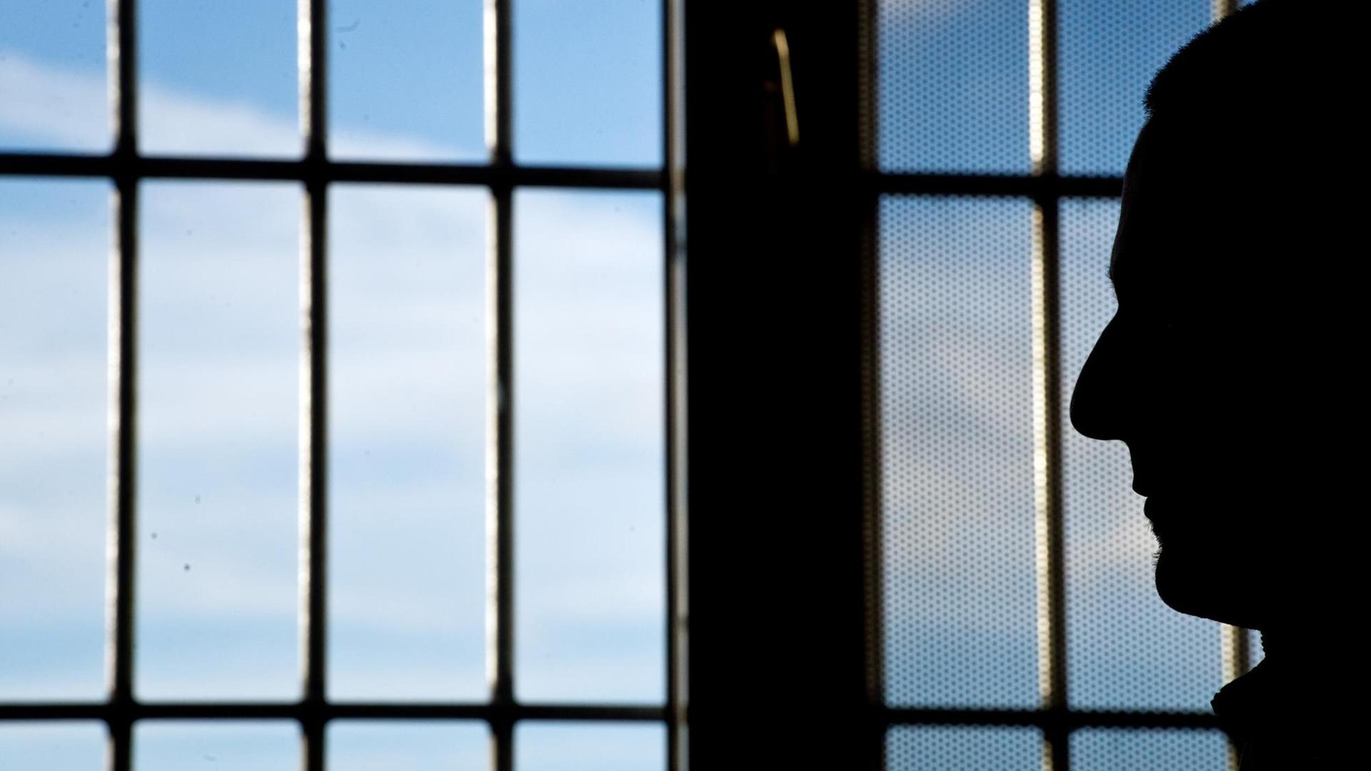 Ein Gefängnisinsasse sitzt vor einem vergitterten Fenster. Ein Gefängnisinsasse sitzt vor einem vergitterten Fenster.