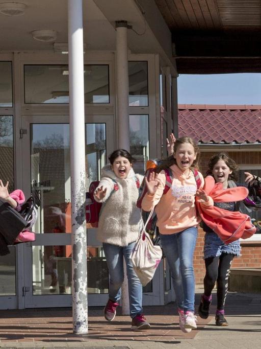 Glückliche Schüler laufen lachend nach Unterrichtsende aus einem Schulgebäude.