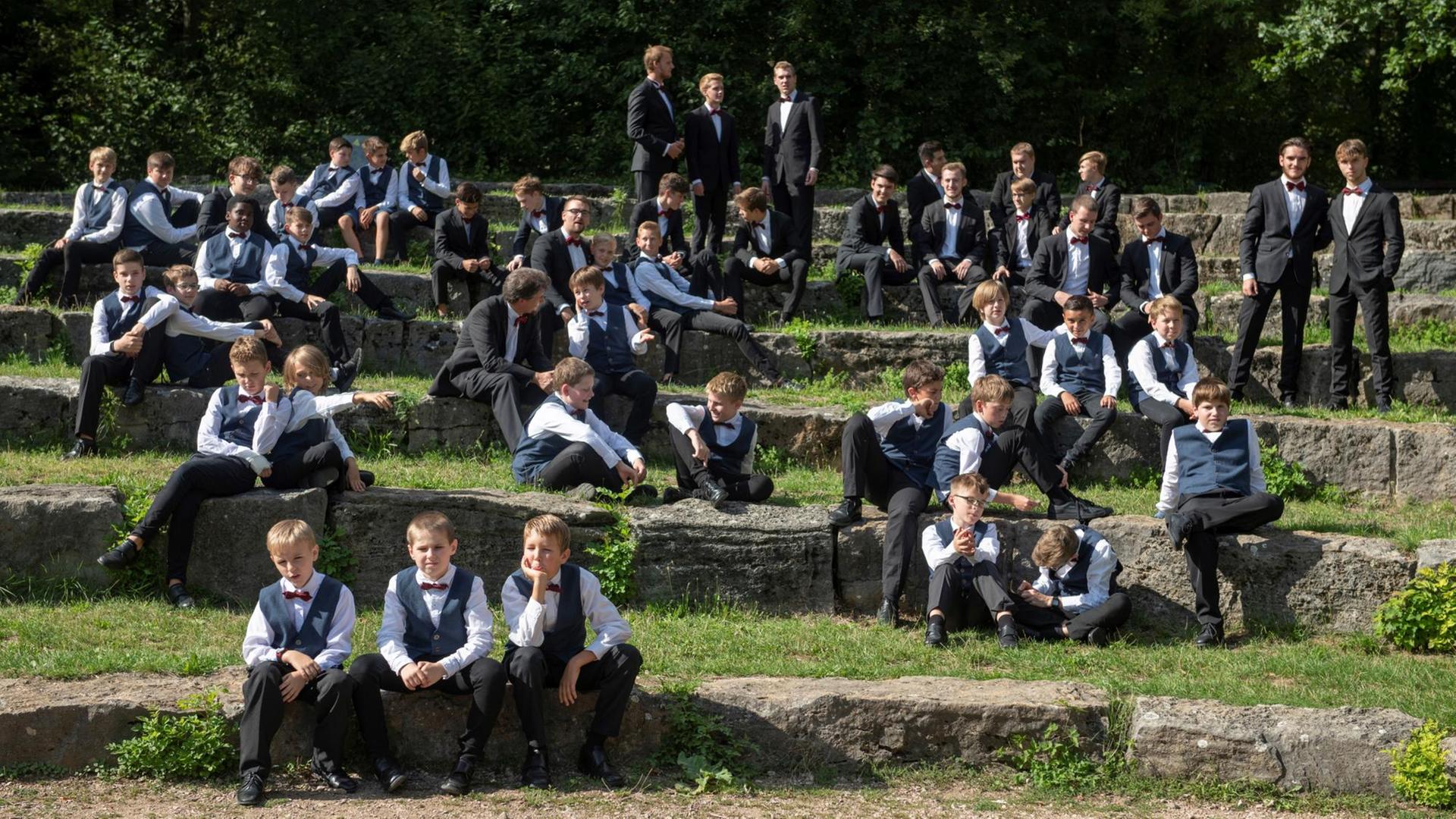 Die Sänger des Chores sitzen oder stehen ungezwungen in kleinen Gruppen in einer felsigen Landschaft. Die Sänger des Chores sitzen oder stehen ungezwungen in kleinen Gruppen in einer felsigen Landschaft.