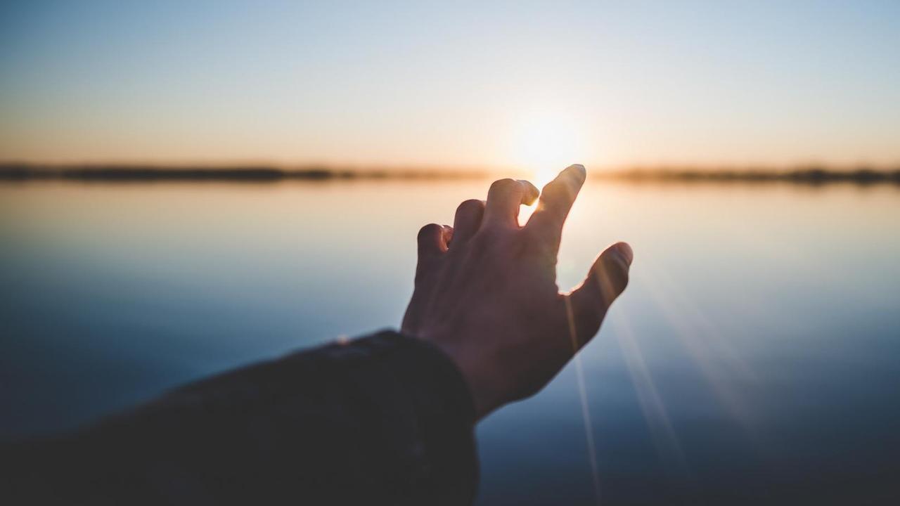 Eine Hand streckt sich in Richtung Horizont und Sonnenlicht. Eine Hand streckt sich in Richtung Horizont und Sonnenlicht.