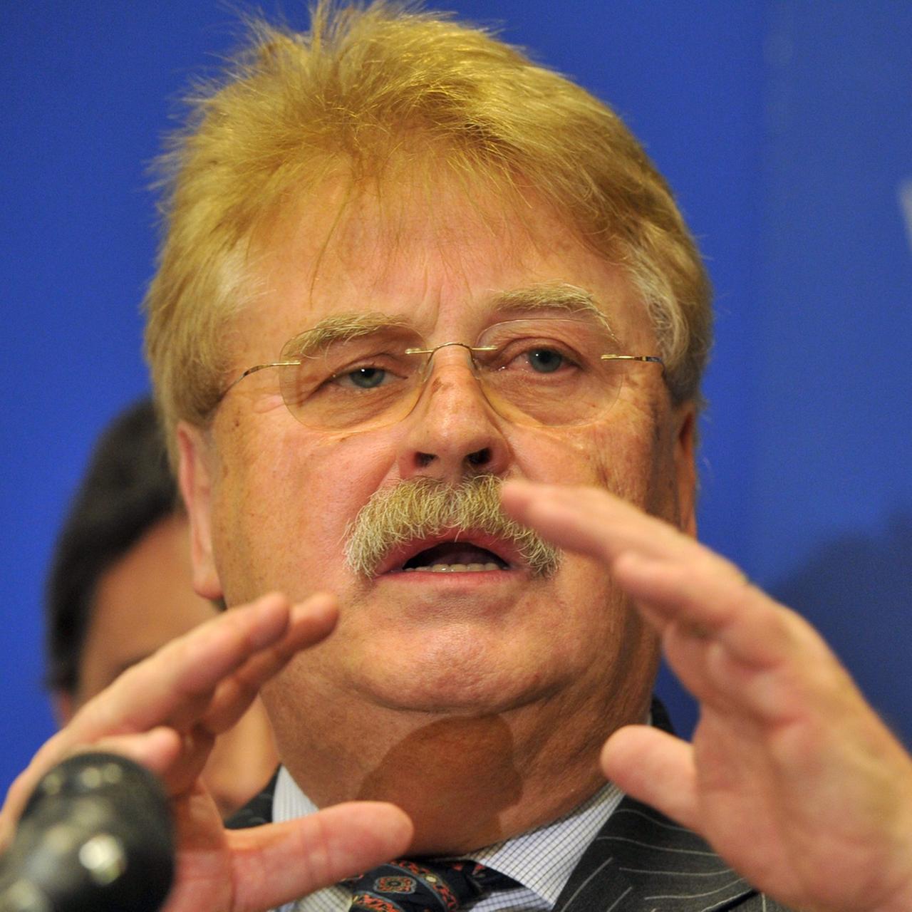 Elmar Brok spricht vor einem Mikrofon, mit den Händen gestikulierend, vor blauem Hintergrund mit weißer kyrillscher Aufschrift. Elmar Brok spricht vor einem Mikrofon, mit den Händen gestikulierend, vor blauem Hintergrund mit weißer kyrillscher Aufschrift.