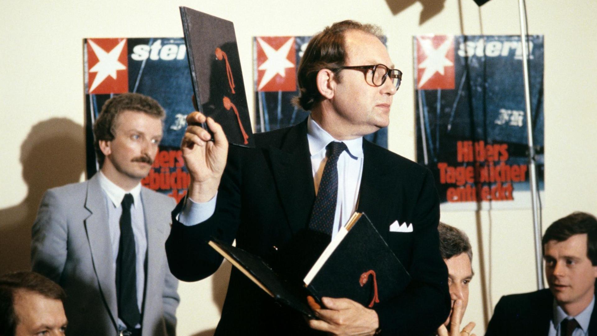 Der Journalist Gerd Heidemann hält bei einer Pressekonferenz im April 1983 ein Exemplar der angeblichen "Hitler-Tagebücher" hoch. Im Hintergrund hängen Titelbilder der "Stern"-Ausgabe zu der Veröffentlichung.