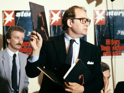 Der Journalist Gerd Heidemann hält bei einer Pressekonferenz im April 1983 ein Exemplar der angeblichen "Hitler-Tagebücher" hoch. Im Hintergrund hängen Titelbilder der "Stern"-Ausgabe zu der Veröffentlichung.