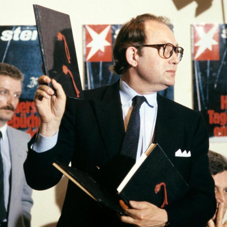 Der Journalist Gerd Heidemann hält bei einer Pressekonferenz im April 1983 ein Exemplar der angeblichen "Hitler-Tagebücher" hoch. Im Hintergrund hängen Titelbilder der "Stern"-Ausgabe zu der Veröffentlichung.