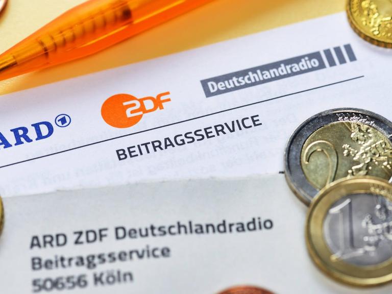 Das Bild zeigt ein Schreiben des Beitragsservices von ARD, ZDF und Deutschlandradio mit den drei Senderlogos. Zu sehen sind zudem Geldmünzen und ein Stift.