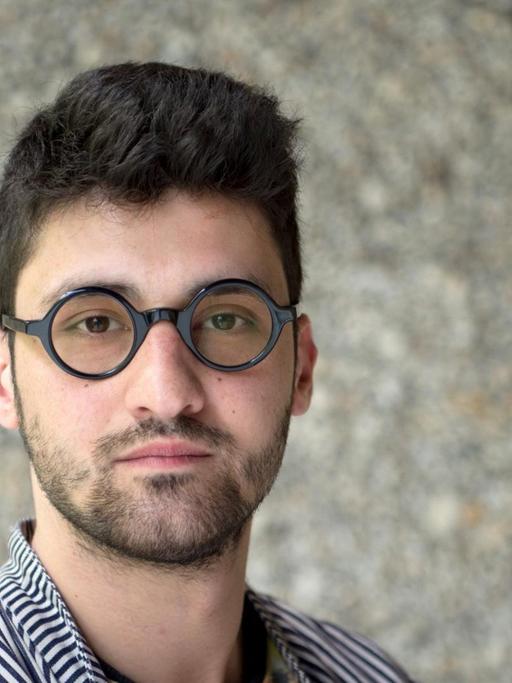 Der Regisseur Ersan Mondtag, aufgenommen vor einer grauen Steinwand
