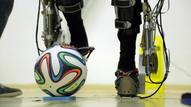 Ein Fußball und zwei Beine, mit Schienen und Kabeln versehen, sind in einem Labor zu sehen