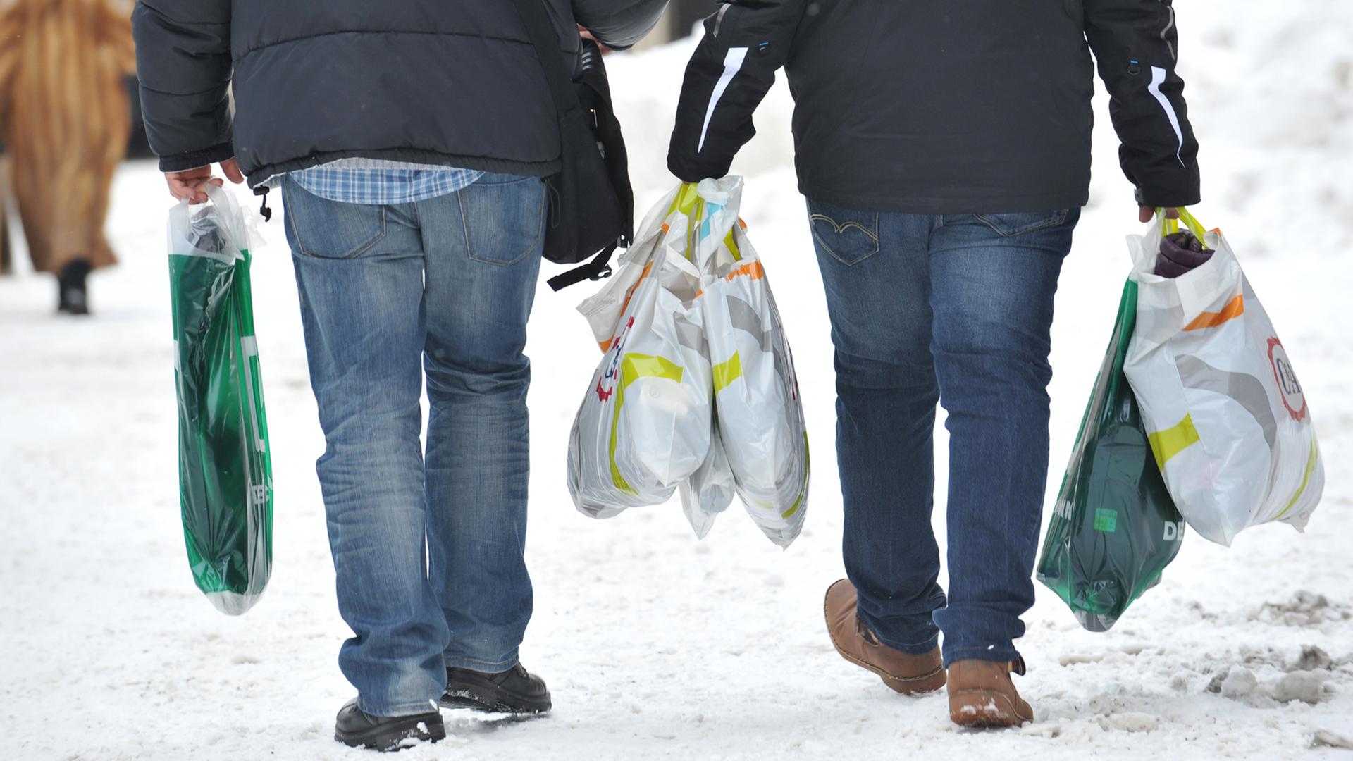 Zwei Männer tragen am 21.01.2013 in der Innenstadt von München (Bayern) mehrere Einkaufstüten.