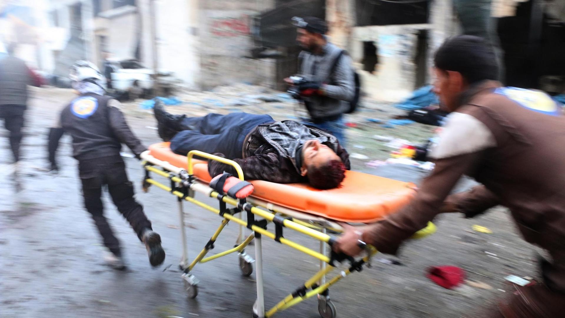 Zwei Helfer bringen in der syrischen Stadt Aleppo einen Verletzten auf einer orangenen Bahre ins Krankenhaus.