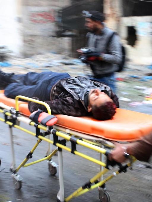 Zwei Helfer bringen in der syrischen Stadt Aleppo einen Verletzten auf einer orangenen Bahre ins Krankenhaus.