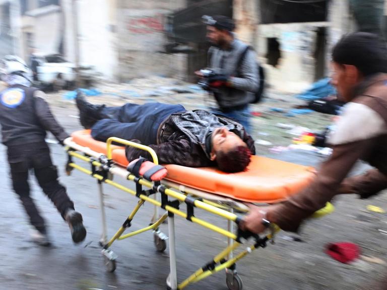 Zwei Helfer bringen in der syrischen Stadt Aleppo einen Verletzten auf einer orangenen Bahre ins Krankenhaus.