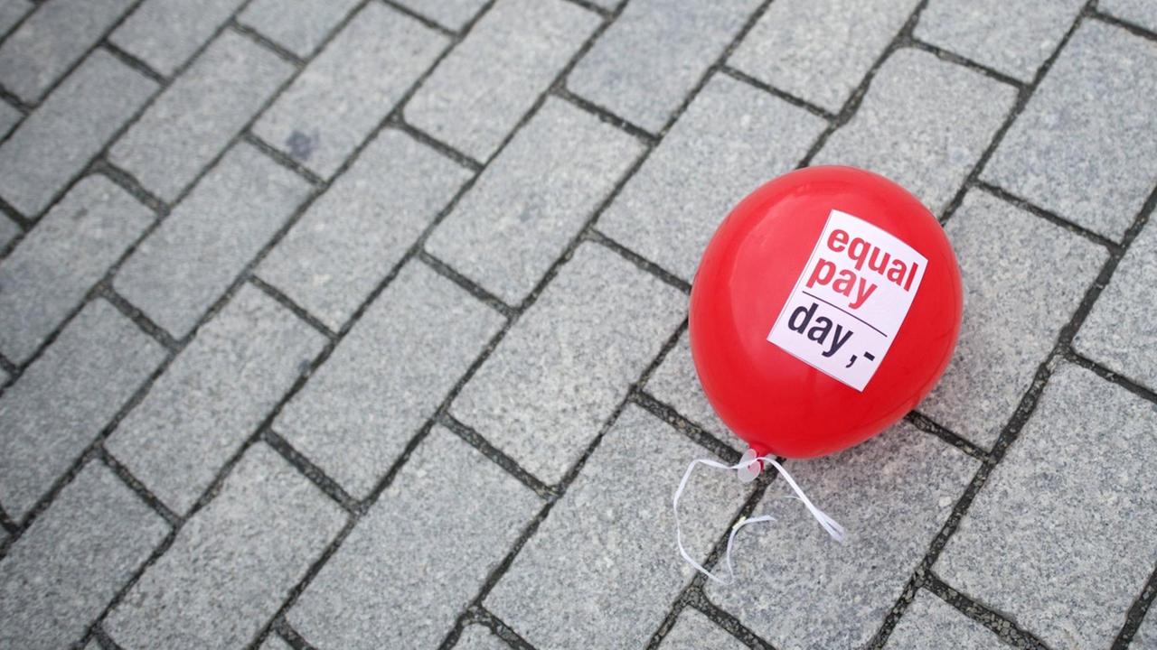 Ein Ballon mit "Equal Pay Day" liegt auf der Straße. Ein Ballon mit "Equal Pay Day" liegt auf der Straße.