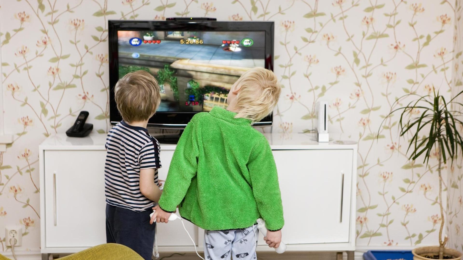 Kinder stehen vor einem Bildschirm und halten Spielekonsolen in den Händen. Kinder stehen vor einem Bildschirm und halten Spielekonsolen in den Händen.