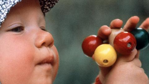 Ein kleines Kind spielt mit einer Rassel aus bunten Holzkugeln.