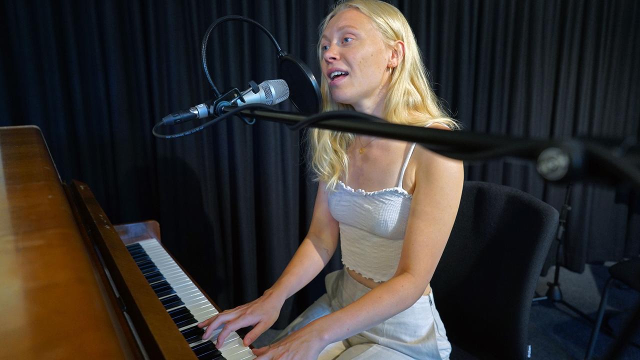Die Musikerin sitzt an einem Klavier und begleitet sich selbst beim Singen. Die Musikerin sitzt an einem Klavier und begleitet sich selbst beim Singen.