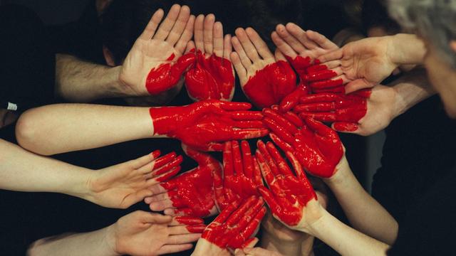 Mehrere Menschen formen mit ihren Handflächen eine größere Fläche, auf das Herz gemalt ist.