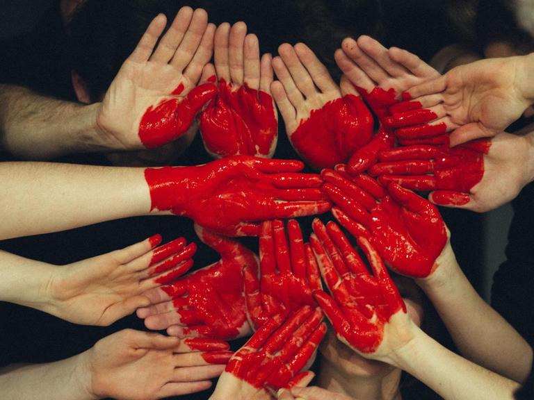 Mehrere Menschen formen mit ihren Handflächen eine größere Fläche, auf das Herz gemalt ist.