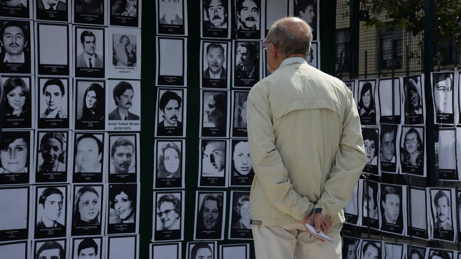 Ein Mann betrachtet schwarzweiß Portraits von Opfern der Militärdiktatur in Argentinien, die vor ihm an einer Wand hängen Ein Mann betrachtet schwarzweiß Portraits von Opfern der Militärdiktatur in Argentinien, die vor ihm an einer Wand hängen