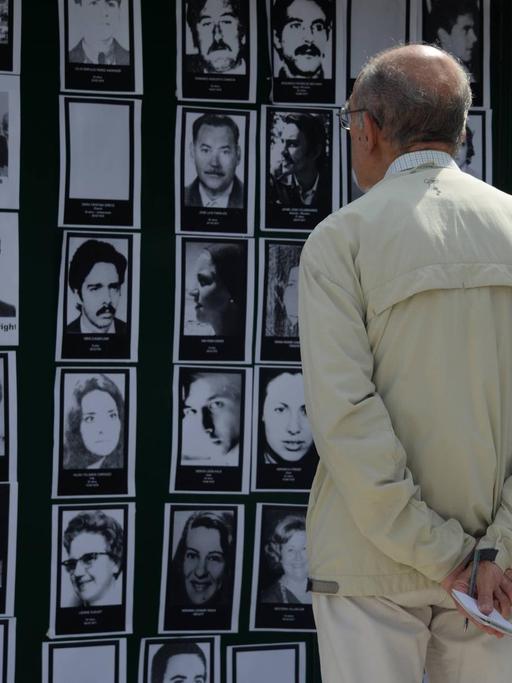 Ein Mann betrachtet schwarzweiß Portraits von Opfern der Militärdiktatur in Argentinien, die vor ihm an einer Wand hängen