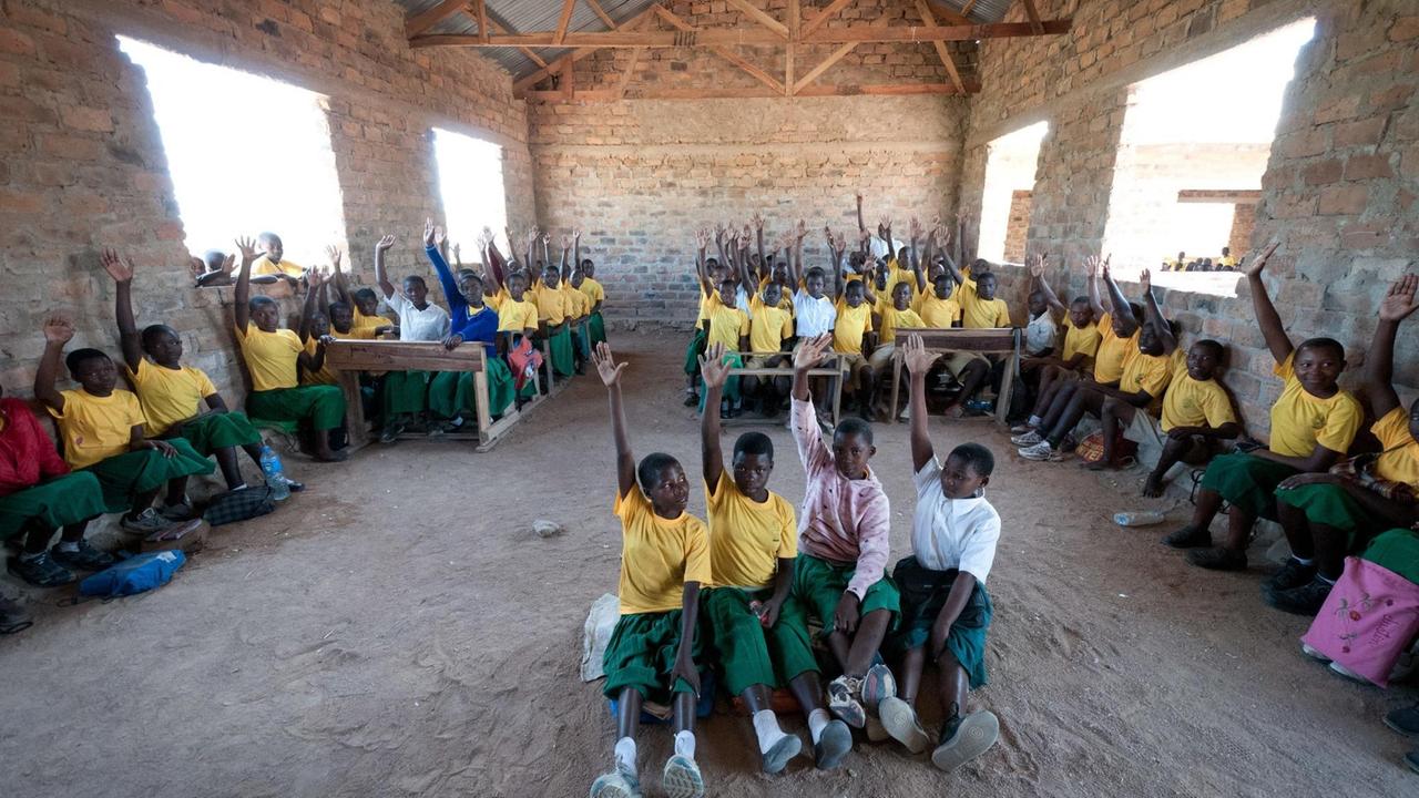 Schülerinnen und Schüler in einem Klassenzimmer, sie tragen gelbe T-Shirts und grüne Hosen. 