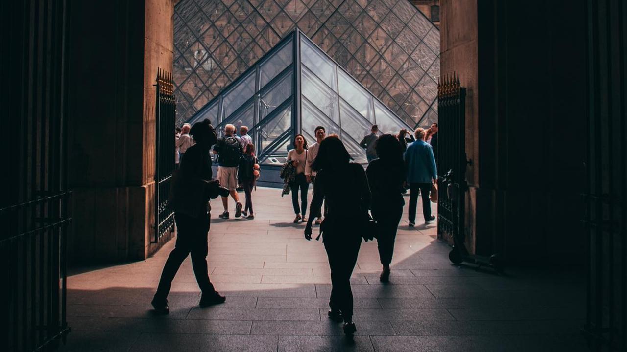 Blick durch einen Torbogen auf die Glaspyramide im Innenhof des Louvre.