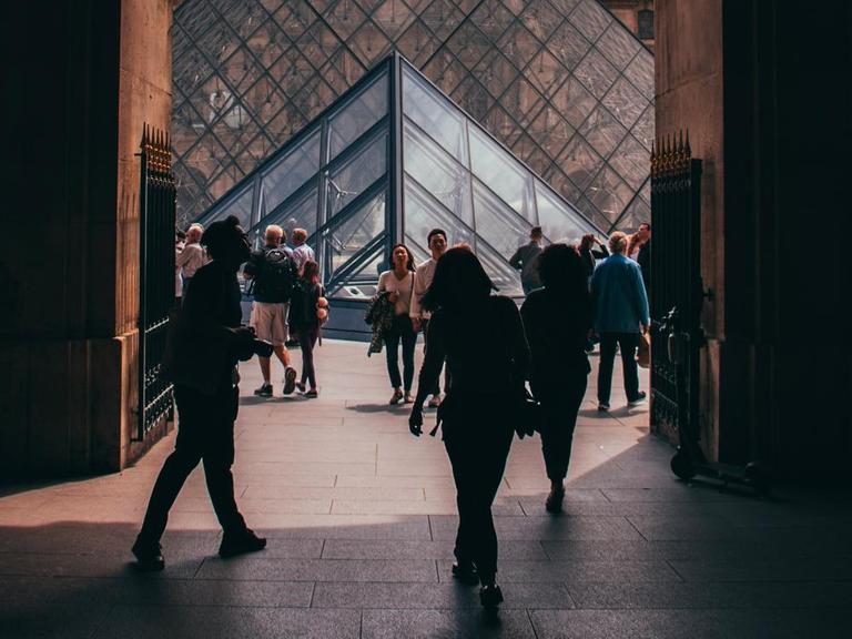 Blick durch einen Torbogen auf die Glaspyramide im Innenhof des Louvre.