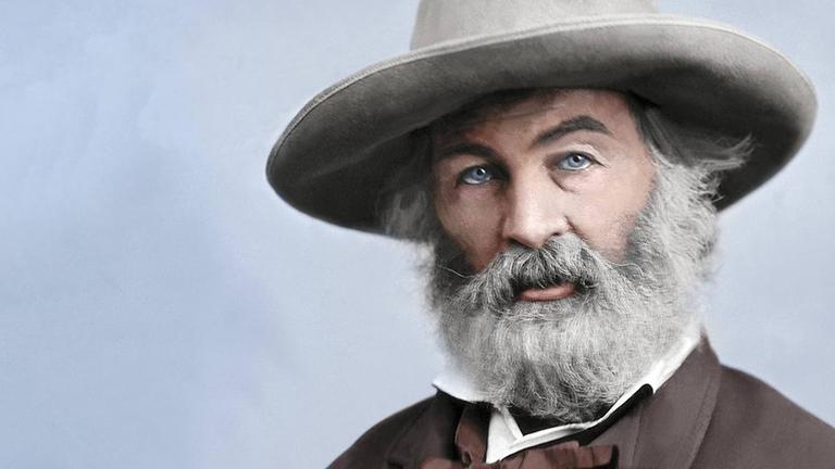 Ein coloriertes Porträt des Dichters Walt Whitman. Er sitzt mit einem Hut mit breiter Krempe auf einen Stuhl und schaut in die Kamera. Seine Hände sind in den Manteltaschen. Ein coloriertes Porträt des Dichters Walt Whitman. Er sitzt mit einem Hut mit breiter Krempe auf einen Stuhl und schaut in die Kamera. Seine Hände sind in den Manteltaschen.