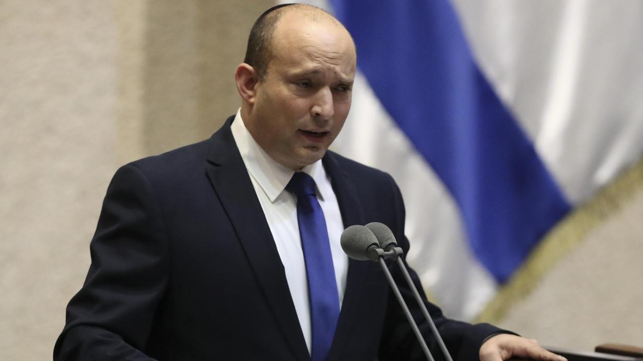 Naftali Bennett steht an einem Redepult und spricht in Mikrofone. Naftali Bennett steht an einem Redepult und spricht in Mikrofone.