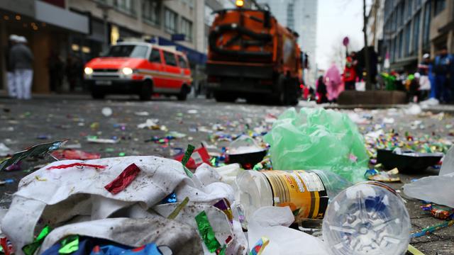 Flaschen, Plastik und anderer Müll liegen auf der Straße. Im Hintergrund steht ein großes Müllfahrzeug bereit.