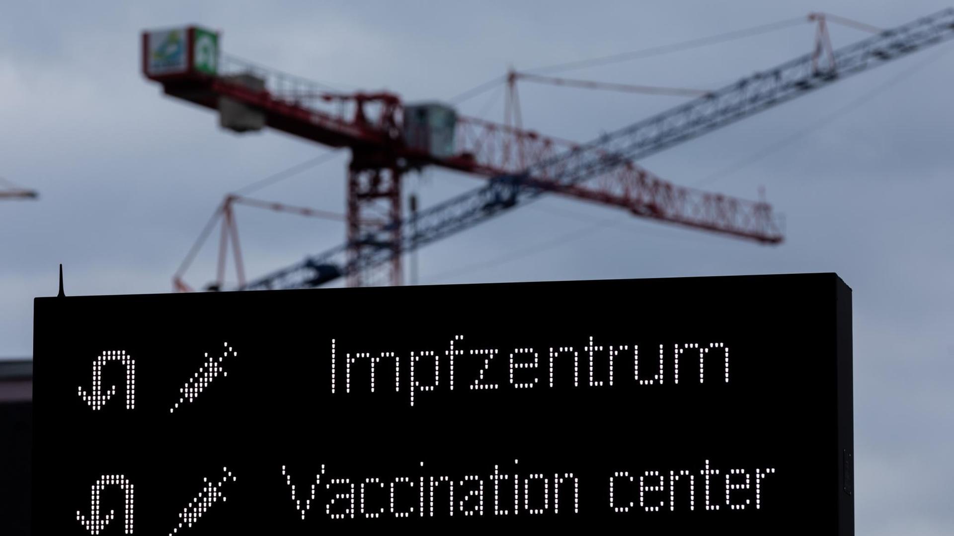 Kräne sind auf einer Baustelle hinter einer Hinweistafel auf den Weg zum Impfzentrum zu sehen. Die Infektionszahlen steigen, gleichzeitig fallen geplante Impfungen mit dem Impfstoff Astrazeneca aus. Kräne sind auf einer Baustelle hinter einer Hinweistafel auf den Weg zum Impfzentrum zu sehen. Die Infektionszahlen steigen, gleichzeitig fallen geplante Impfungen mit dem Impfstoff Astrazeneca aus.