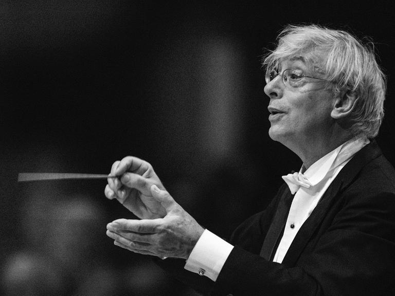 Der Dirigent Mario Venzago hält einen Taktstock in der Hand und blickt zum Orchester.