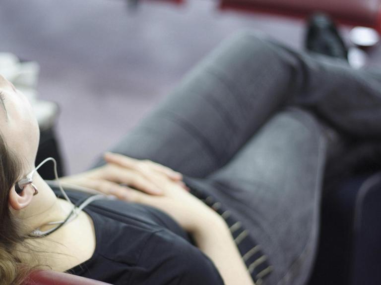 Eine junge Frau zurückgelehnt auf einem Stuhl hört Musik