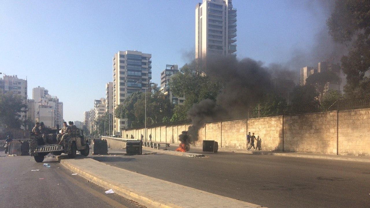 Auf einer Straße ist eine Barrikade errichtet, ein Teil davon brennt. Im Hintergrund sind Hochhäuser zu sehen.
