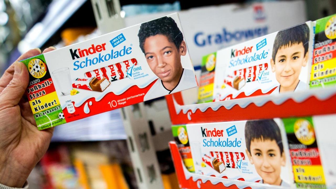 Eine Hand Hält eine Schachtel Kinderschokolade mit dem Kinderbild von Jerome Boateng vor einem Regal im Supermarkt in der Hand. Eine Hand Hält eine Schachtel Kinderschokolade mit dem Kinderbild von Jerome Boateng vor einem Regal im Supermarkt in der Hand.