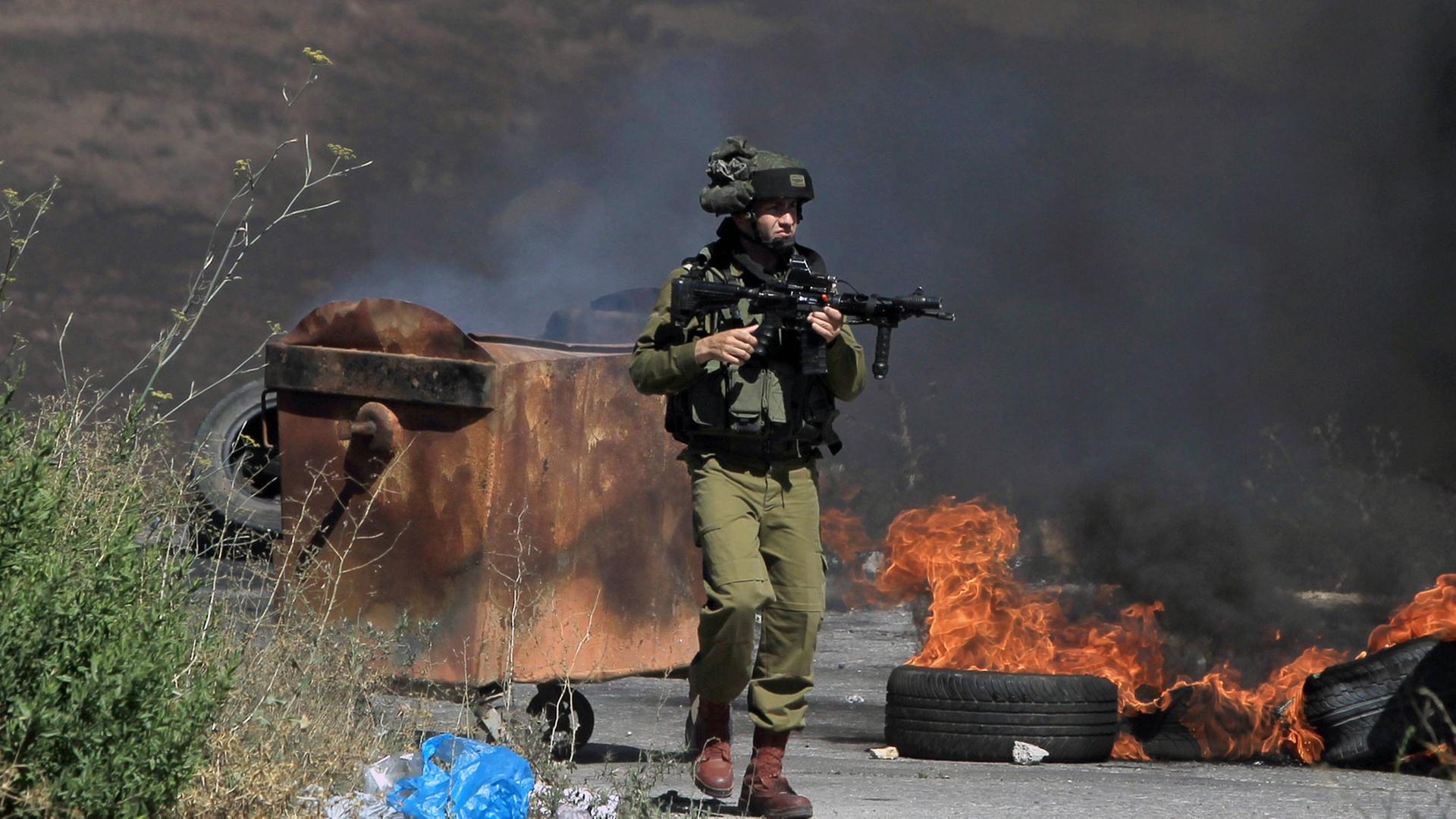 Ein bewaffneter israelischer Soldat steht neben brennenden Reifen während Auseinandersetzungen mit Palästinensern nahe einer jüdischen Siedlung bei Ramallah.