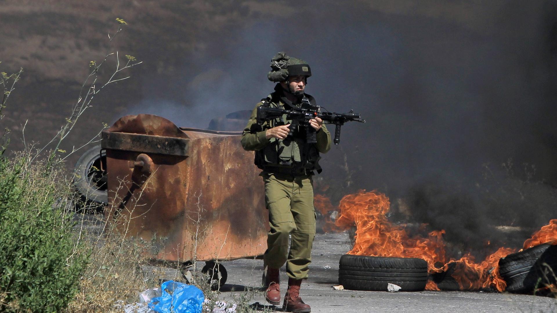 Ein bewaffneter israelischer Soldat steht neben brennenden Reifen während Auseinandersetzungen mit Palästinensern nahe einer jüdischen Siedlung bei Ramallah. Ein bewaffneter israelischer Soldat steht neben brennenden Reifen während Auseinandersetzungen mit Palästinensern nahe einer jüdischen Siedlung bei Ramallah.