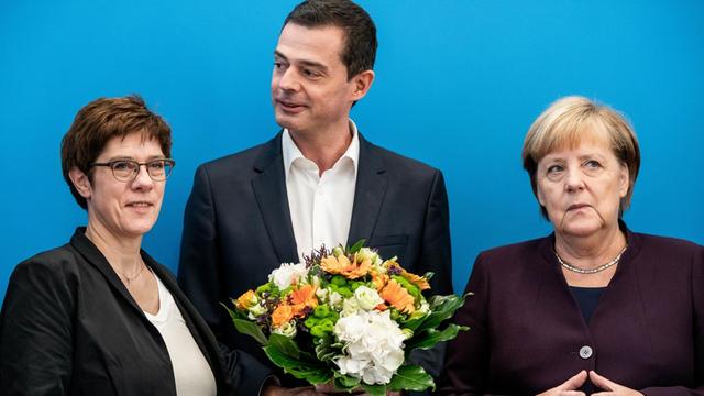 Mike Mohring, Landesvorsitzender der CDU in Thüringen, steht mit seinem Blumenstrauß zwischen Annegret Kramp-Karrenbauer (l.), Bundesvorsitzende der CDU und Verteidigungsministerin, und Bundeskanzlerin Angela Merkel (CDU).