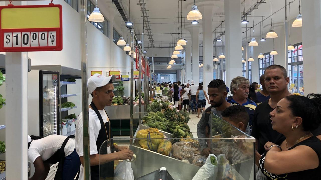 Ein Obststand in der Markthalle unter anderem mit Bananen. Eine Frau bezahlt. Hinter ihr bildet sich eine Schlange. Ein Obststand in der Markthalle unter anderem mit Bananen. Eine Frau bezahlt. Hinter ihr bildet sich eine Schlange.