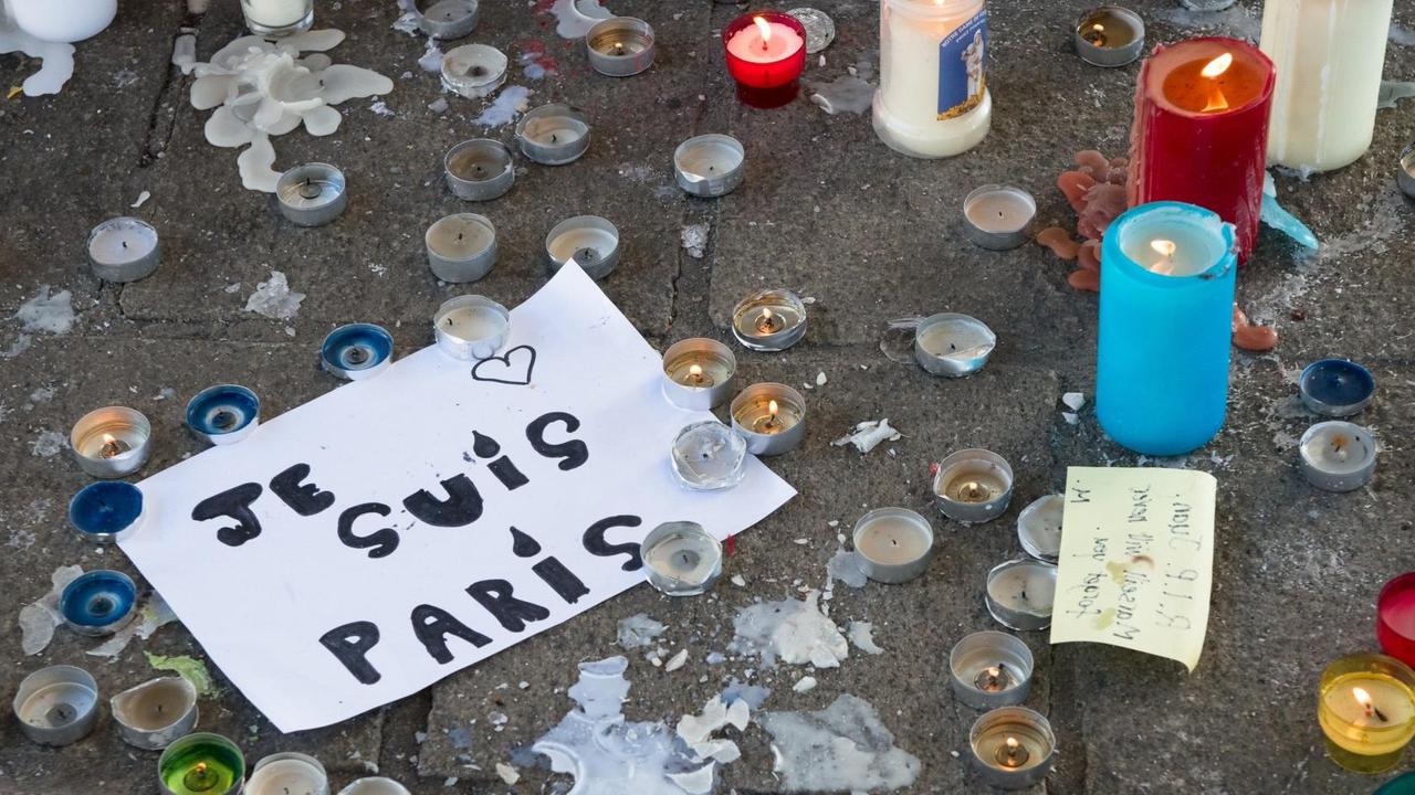 Zu sehen sind viele Teelichter, und der Schriftzug "Je suis Paris" auf einem Blatt Papier. Zu sehen sind viele Teelichter, und der Schriftzug "Je suis Paris" auf einem Blatt Papier.