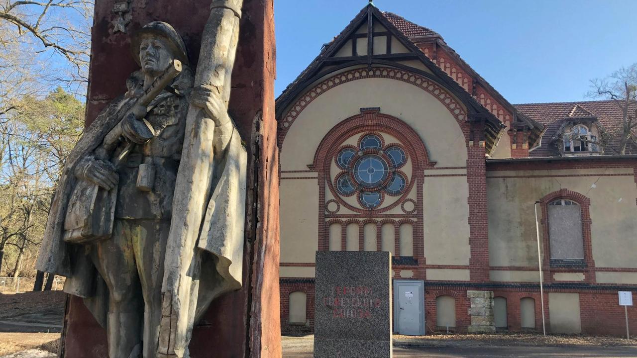 Die Steinskulptur zeigt einen sowjetischen Militärsanitäter, der ein Gewehr vor sich hält. Im Hintergrund ein Gebäude, bei dem einige Scheiben kaputt sind. Die Steinskulptur zeigt einen sowjetischen Militärsanitäter, der ein Gewehr vor sich hält. Im Hintergrund ein Gebäude, bei dem einige Scheiben kaputt sind.