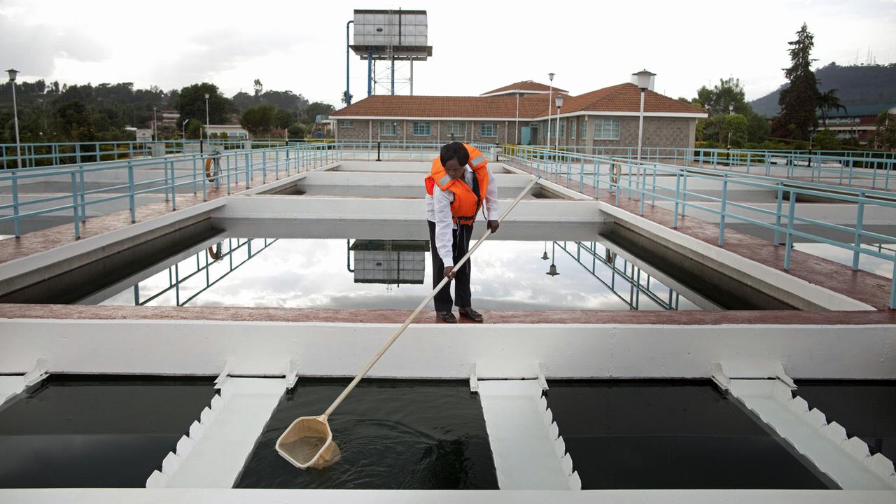 Eine Frau in Sicherheitsweste entfernt Schmutz aus einem Wasserbecken in einem Pumpwerk in Nyeri in Kenia, aufgenommen 2012. Eine Frau in Sicherheitsweste entfernt Schmutz aus einem Wasserbecken in einem Pumpwerk in Nyeri in Kenia, aufgenommen 2012.