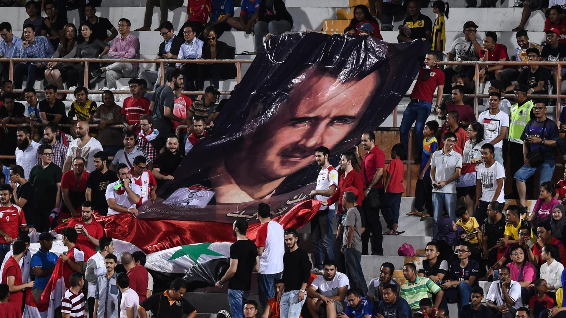 Syrische Fußballfans zeigen ein Porträt des syrischen Präsidenten Bashar al-Assad während des Qualifikationsfußballspiels der Fußball-Weltmeisterschaft 2018 zwischen Südkorea und Syrien (Archivbild 2016) Syrische Fußballfans zeigen ein Porträt des syrischen Präsidenten Bashar al-Assad während des Qualifikationsfußballspiels der Fußball-Weltmeisterschaft 2018 zwischen Südkorea und Syrien (Archivbild 2016)