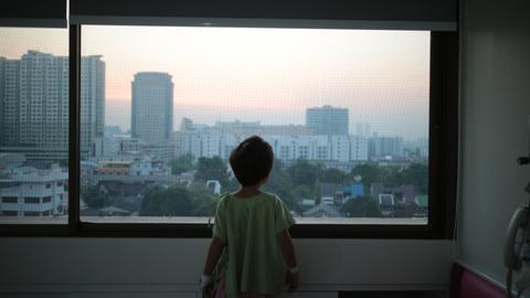 Ein Kind schaut aus einem Fenster auf Hochhäuser.