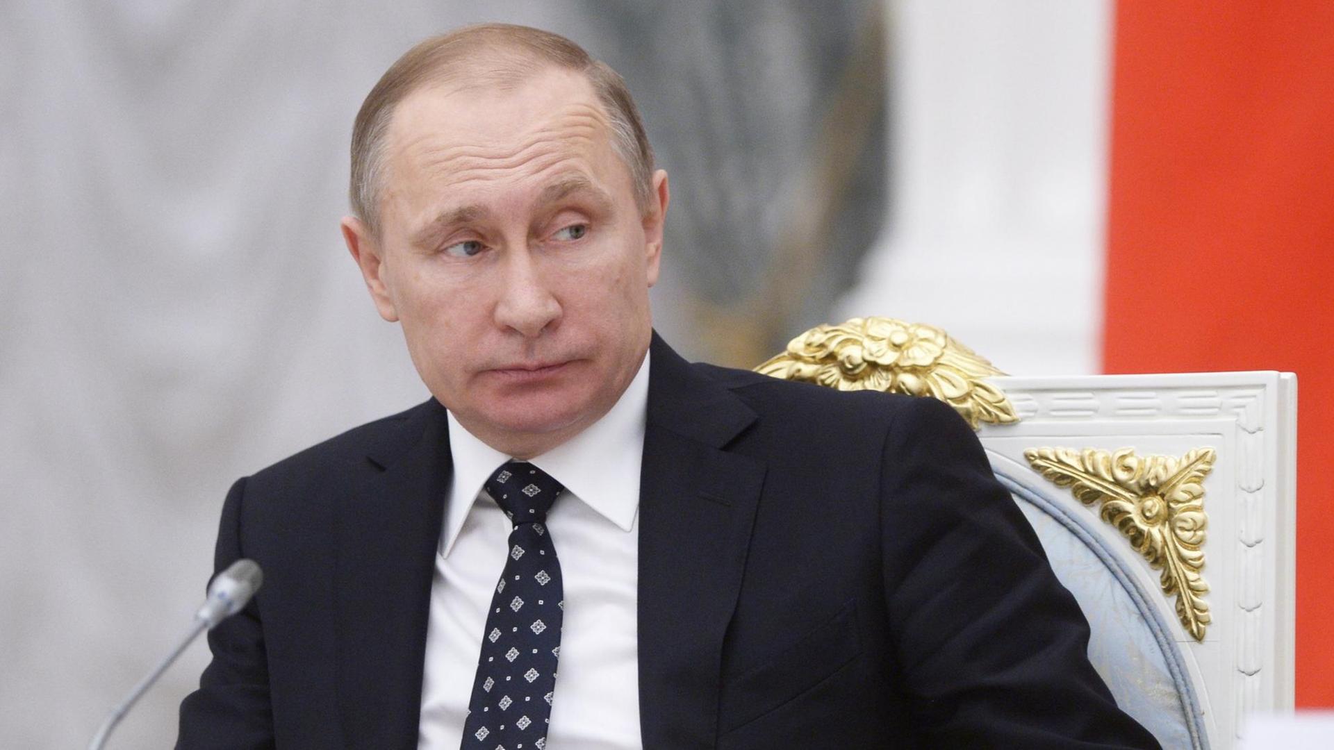 Russlands Präsident Putin sitzt im Kreml vor einem Mikrofon und blickt zur Seite Russlands Präsident Putin sitzt im Kreml vor einem Mikrofon und blickt zur Seite