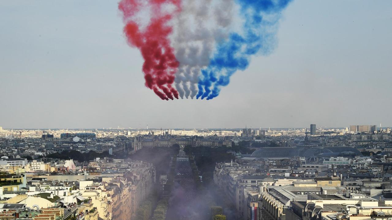 Flugzeuge fliegen über den Boulevard Champs Elysee und hinterlassen Streifen in den Farben der Trikolore am Himmel.