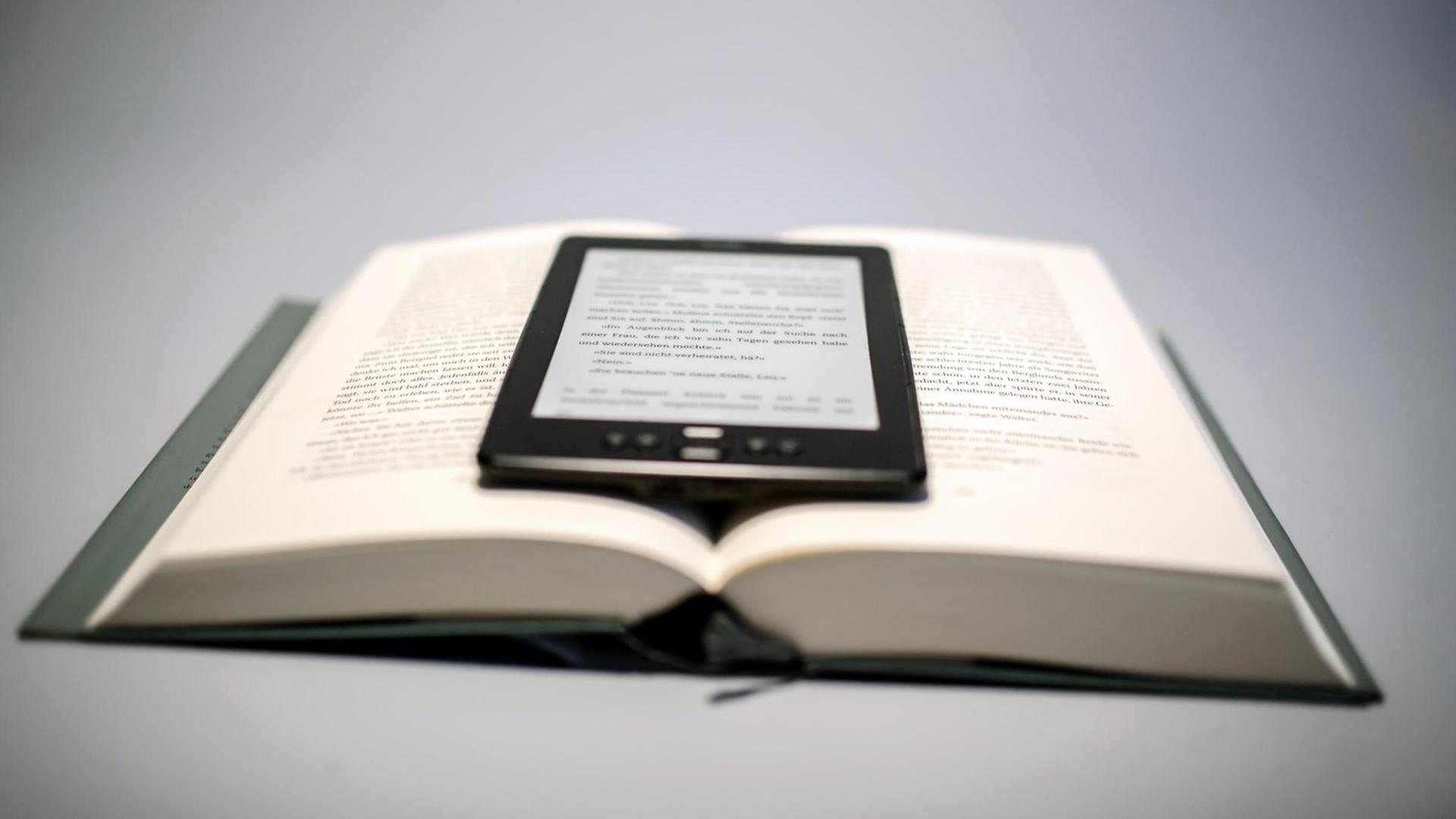 Ein E-Book-Reader liegt auf einem aufgeschlagenen Buch Ein E-Book-Reader liegt auf einem aufgeschlagenen Buch