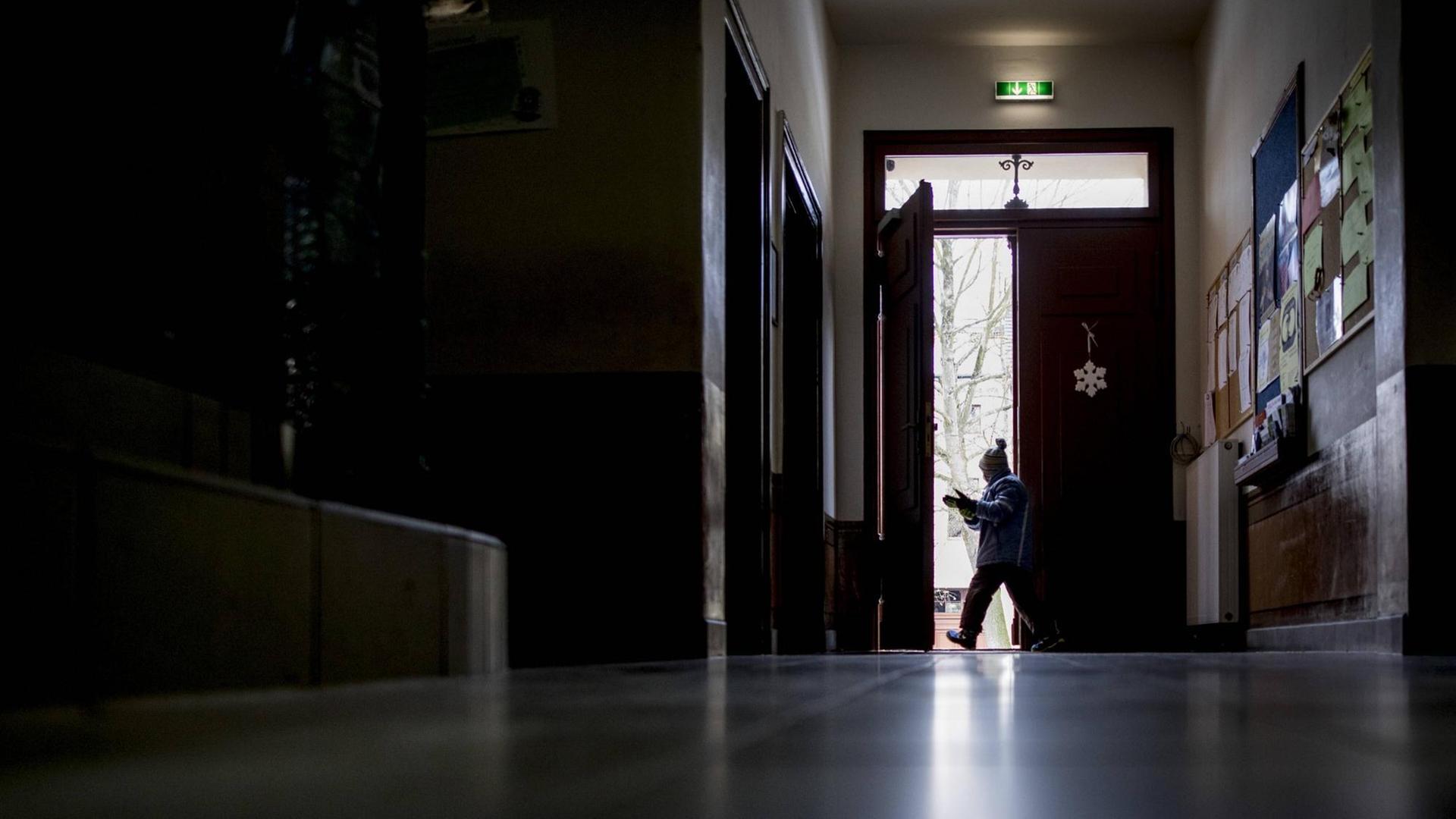Blick durch den Gang einer Schule. Ein Schüler verlässt das Gebäude durch eine Tür am Ende des Gangs Blick durch den Gang einer Schule. Ein Schüler verlässt das Gebäude durch eine Tür am Ende des Gangs