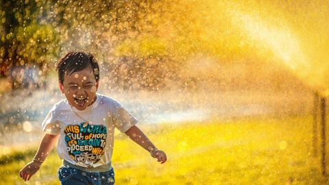 Ein kleiner Junge rennt begeistert unter dem Wassernebel einer Sprenkleranlage her
