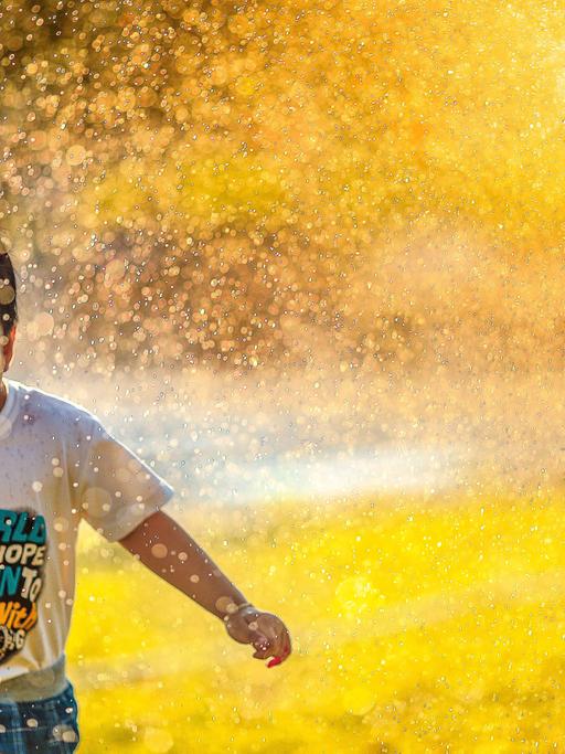 Ein kleiner Junge rennt begeistert unter dem Wassernebel einer Sprenkleranlage her